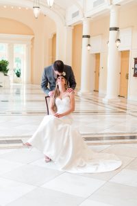 Bride Sitting on Chair, looking up at her groom.