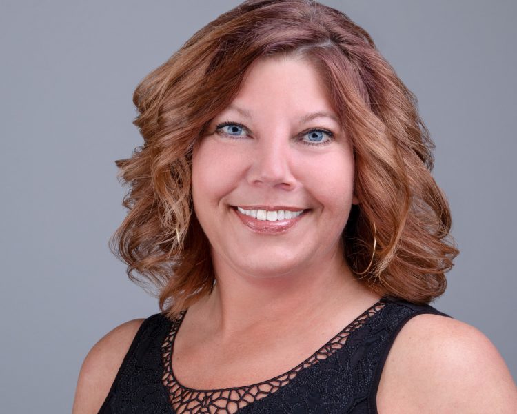 Business Headshot of a woman on a grey background.